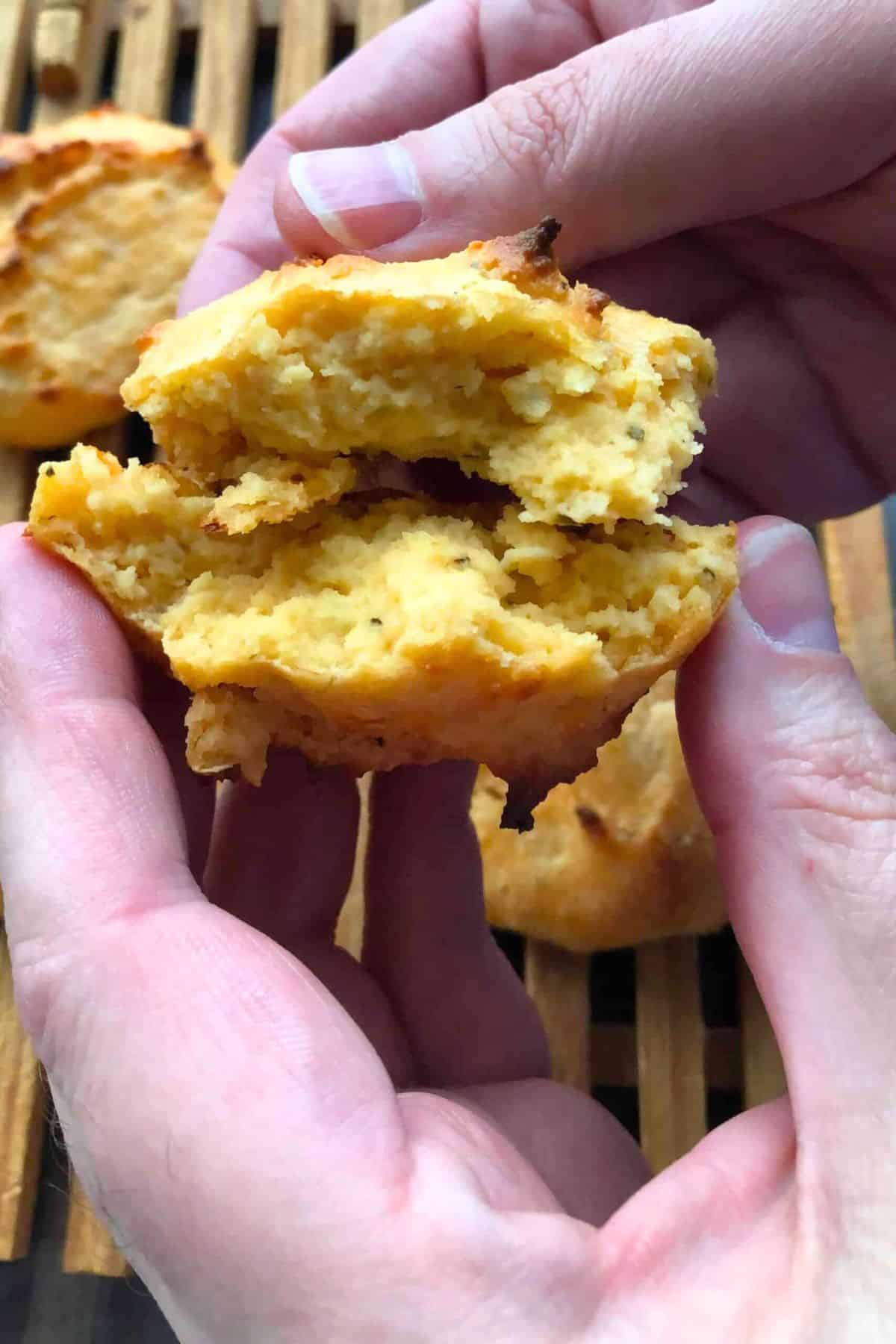 Sugar free biscuits on a bread cutting board while showing two hands breaking a biscuit in half.