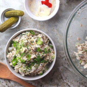 white bowl with chicken salad topped with sliced green onions next to pickles and mayo.