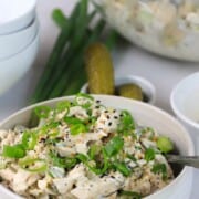 white bowl with chicken salad topped with sliced green onions next to pickles and green onions.