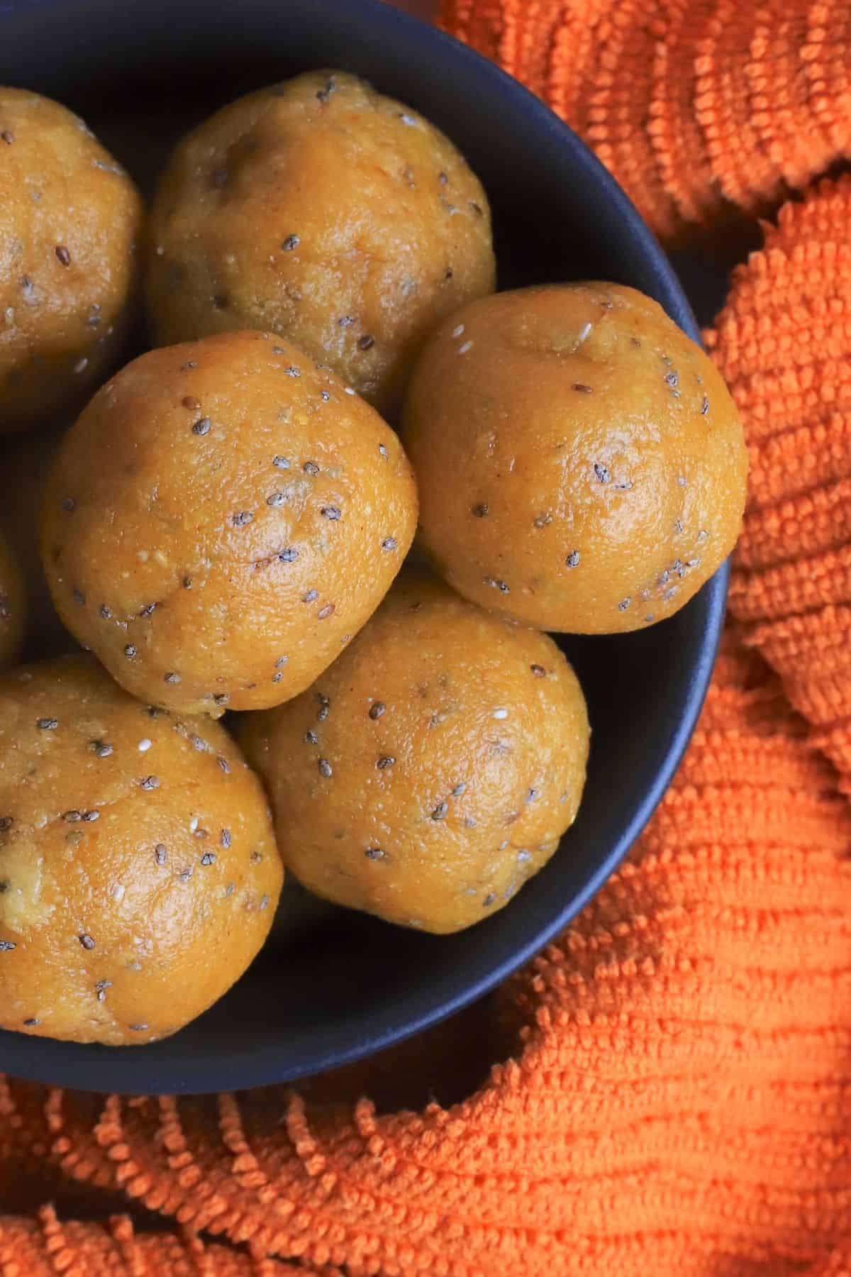 A closeup of a bowl of pumpkin protein balls in a black bowl on an orange towel.