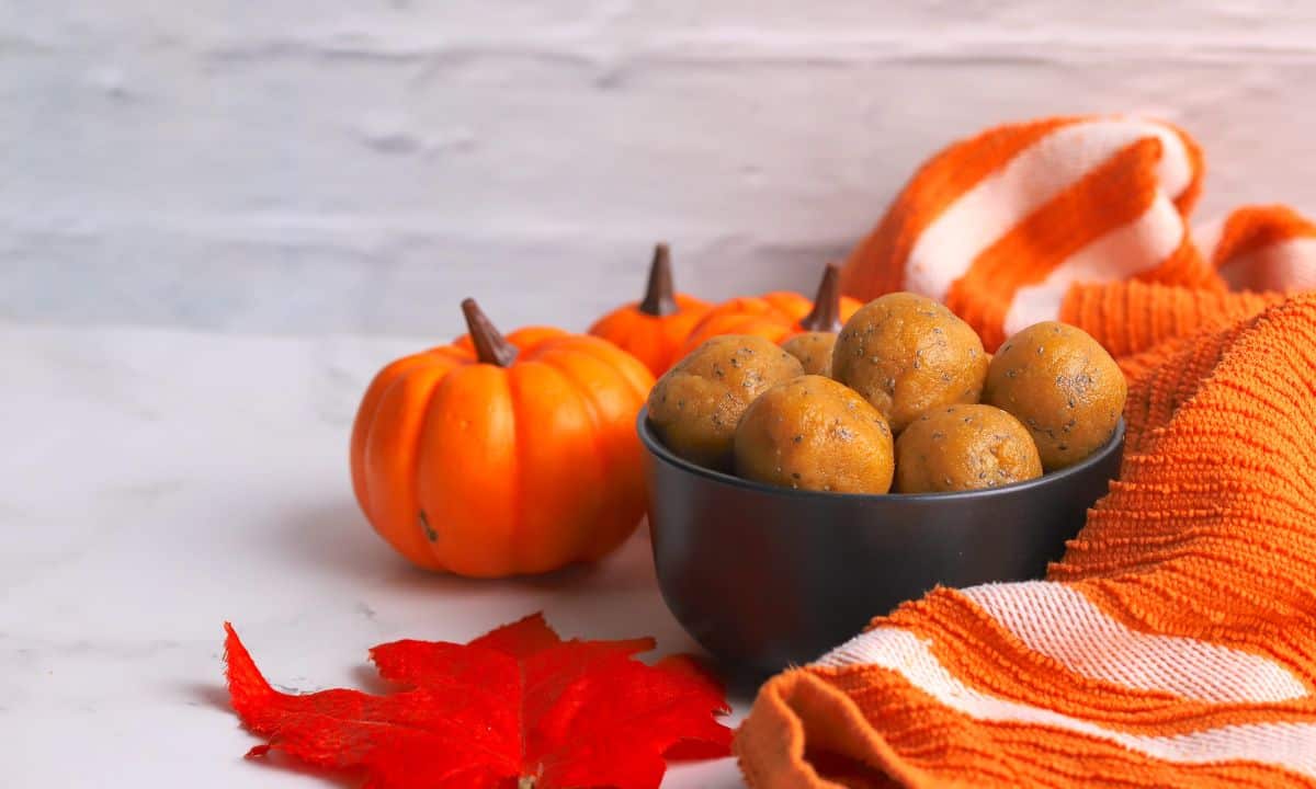A bowl of pumpkin protein balls surrounded by small pumpkins, an orange leaf and an orange towel.