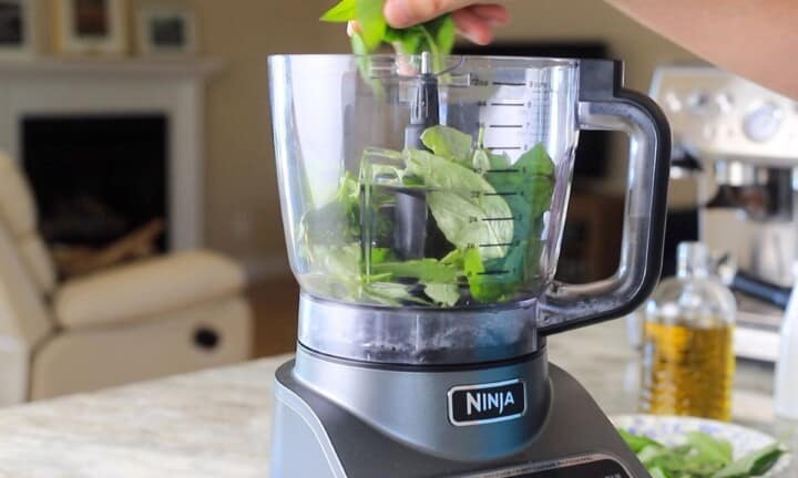 Adding basil leaves to the food processor.