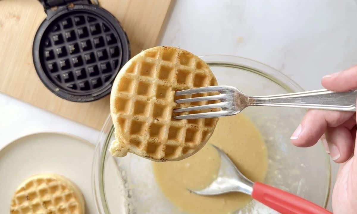 waffle being held up with a fork above the waffle iron.