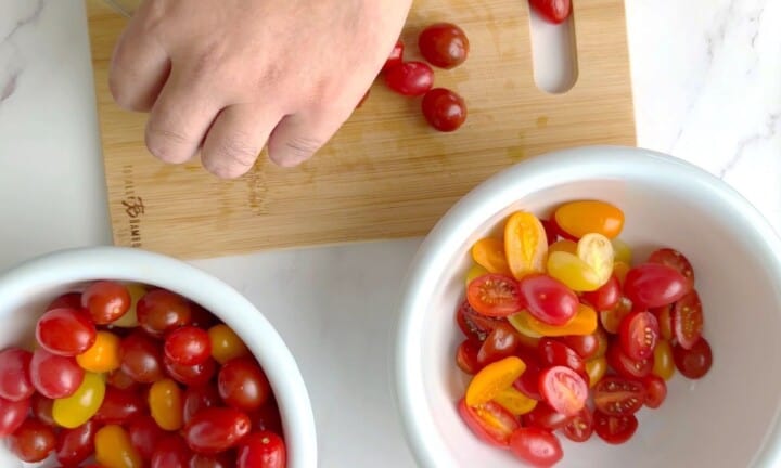 Cutting the cherry tomatoes on a cutting board.
