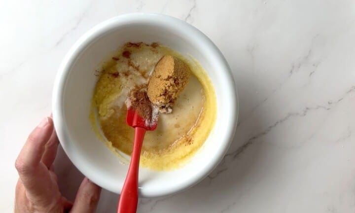 Mixing the filling for the apple crips in a white bowl with a red spatula.