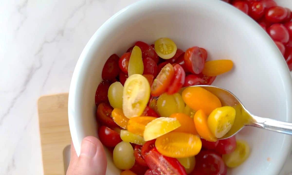 Mixing the cherry tomatoes in a white bowl.