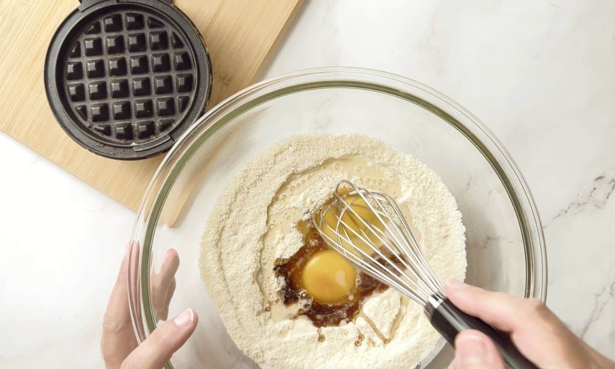 mixing the waffle batter in a glass bowl next to the waffle iron.