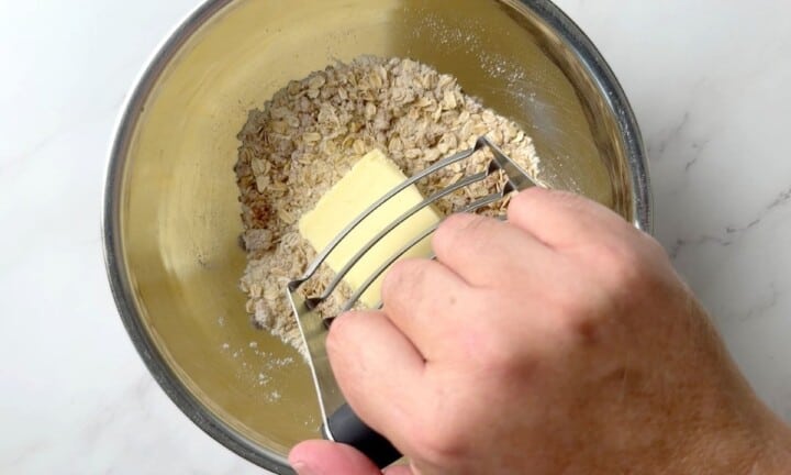 Using a pastry cutter to cut the butter in the bowl of apple crisp topping.