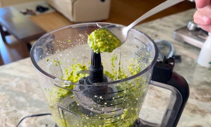 A spoon with the basil pesto above the open food processor.