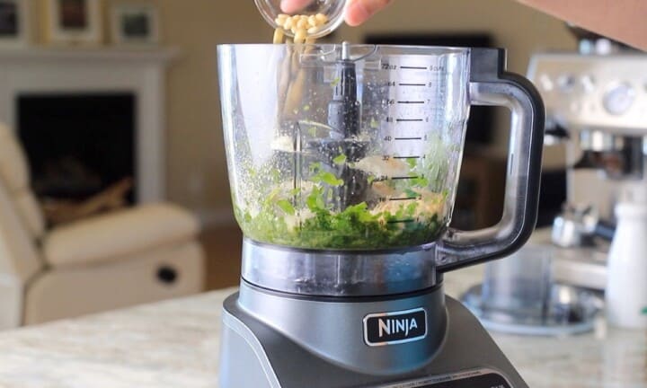 Adding pine nuts to the food processor.