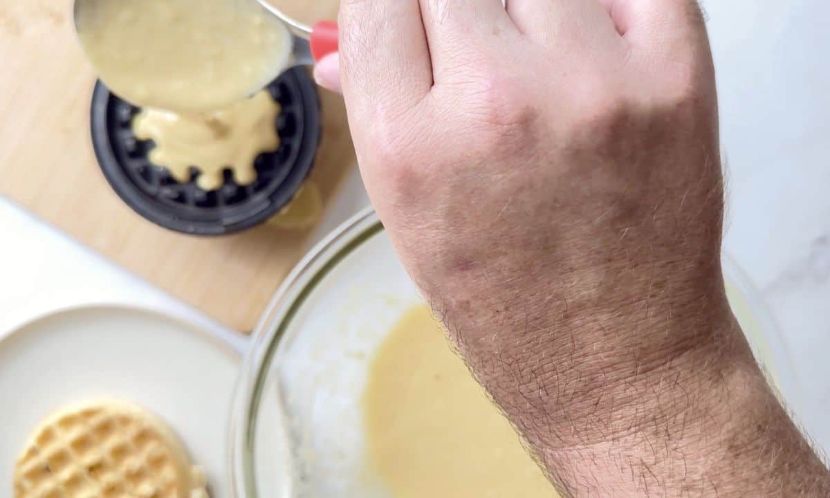 pouring the waffle batter onto the waffle iron with a spoon.