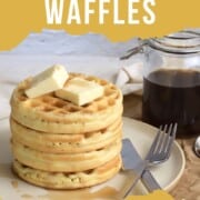 stack of protein powder waffles on a plate with a knife and fork next to a jar with syrup.