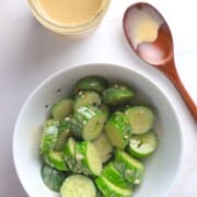Bowl of cucumber salad mixed with the roasted sesame dressing next to a jar with the dressing and a wooden spoon.