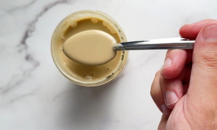 Sugar free salad dressing in a jar with a spoon above filled with the dressing.