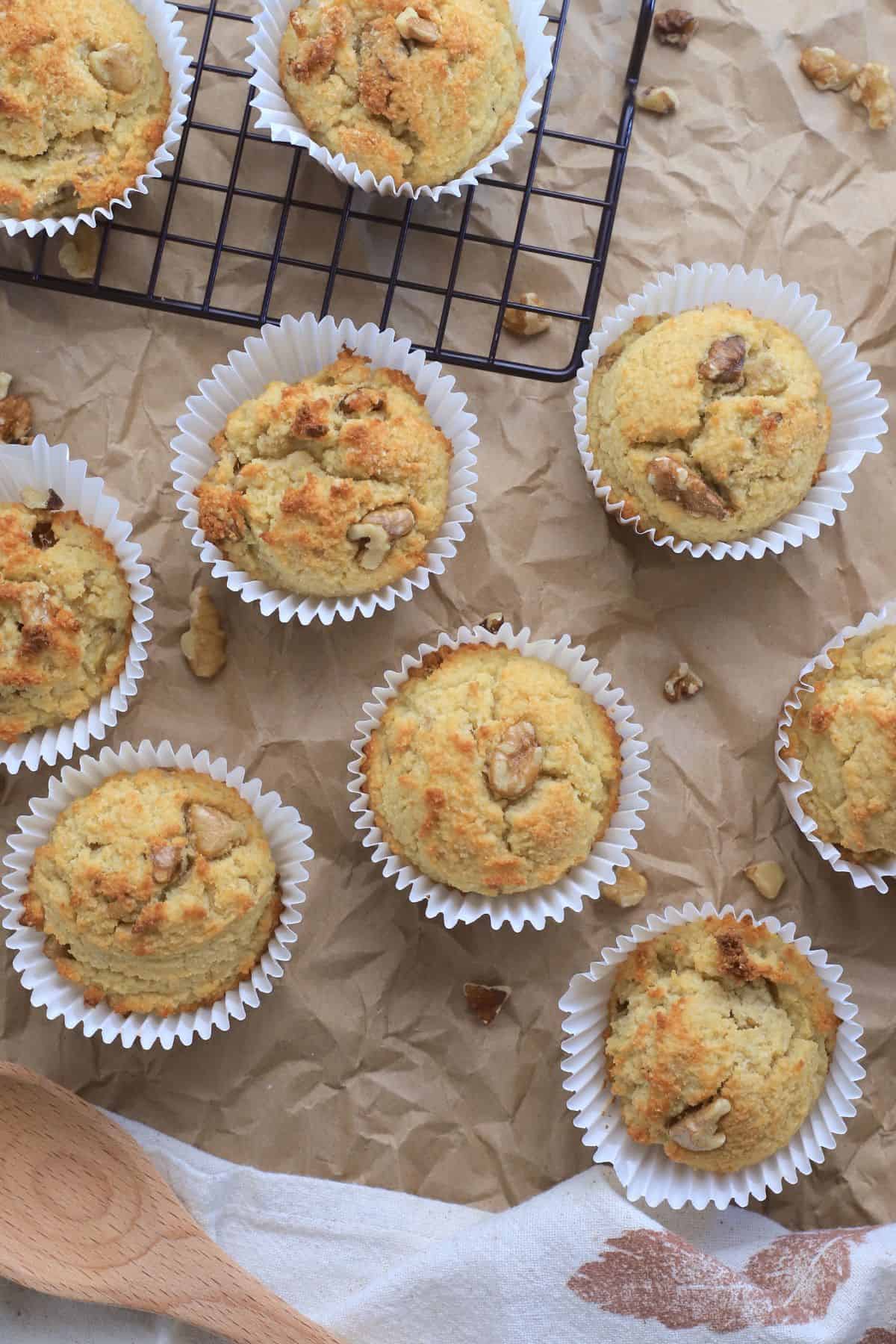 sugar free banana muffins on a brown parchment paper with scattered walnut piecces and a wooden spoon.