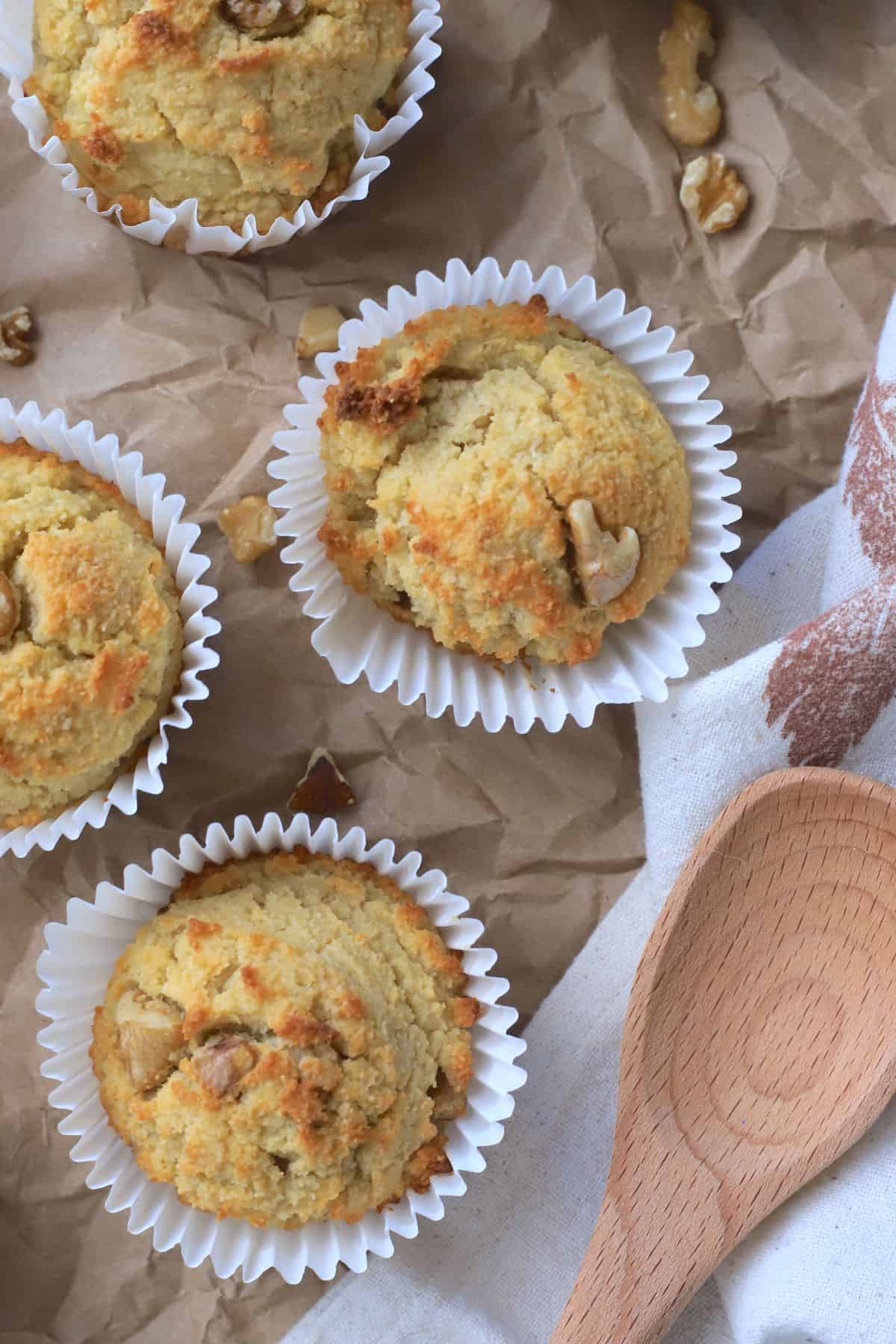 sugar free banana muffins on a brown parchment paper with scattered walnut piecces and a wooden spoon.