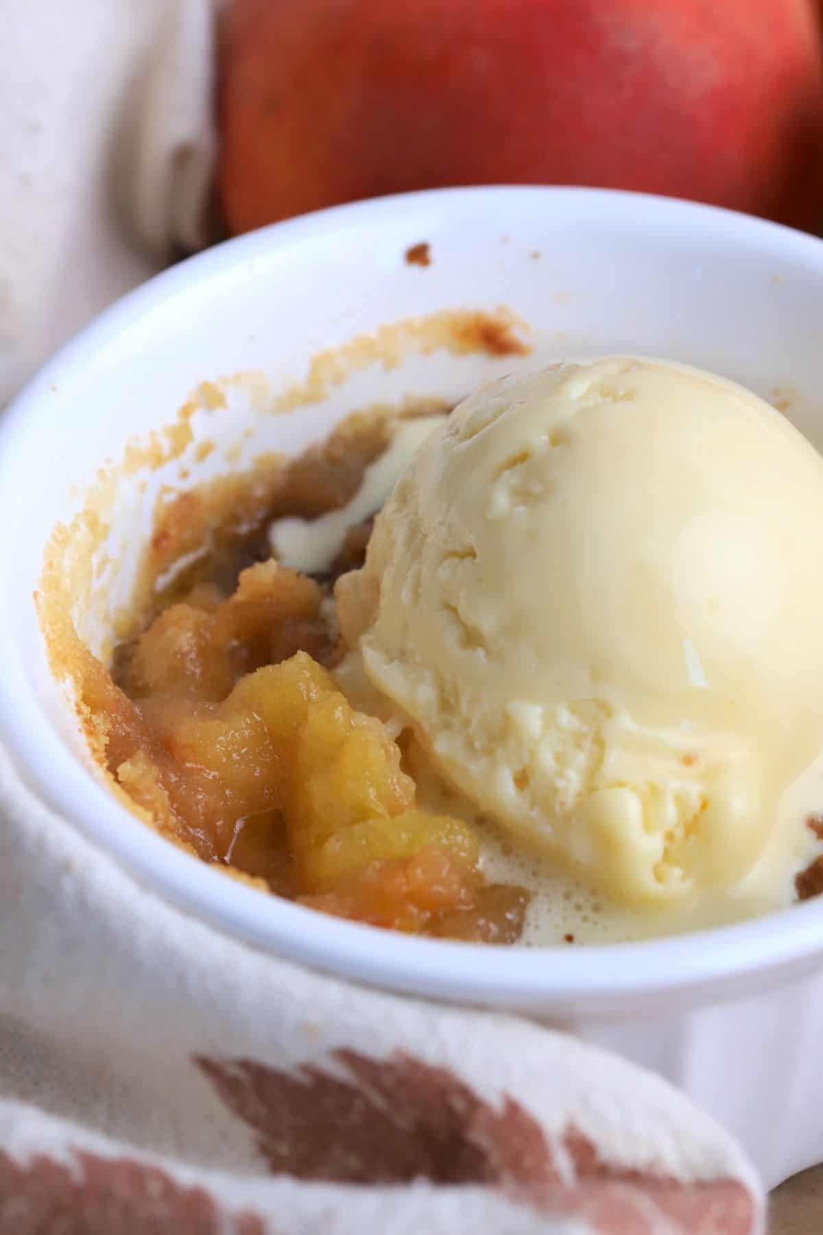 Close up of a peach cobbler in a ramekin dish topped with a scoop of vanilla ice cream.