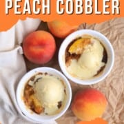 Two peach cobblers in individual ramekins topped with vanilla ice cream and surrounded by 3 fresh peaches.