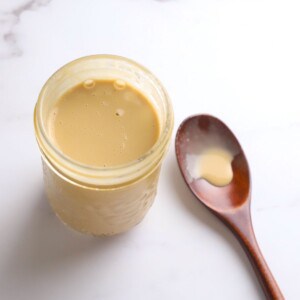 Sugar free salad dressing in a jar next to a wooden spoon.