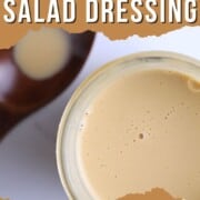 Sugar free salad dressing in a jar next to a wooden spoon.