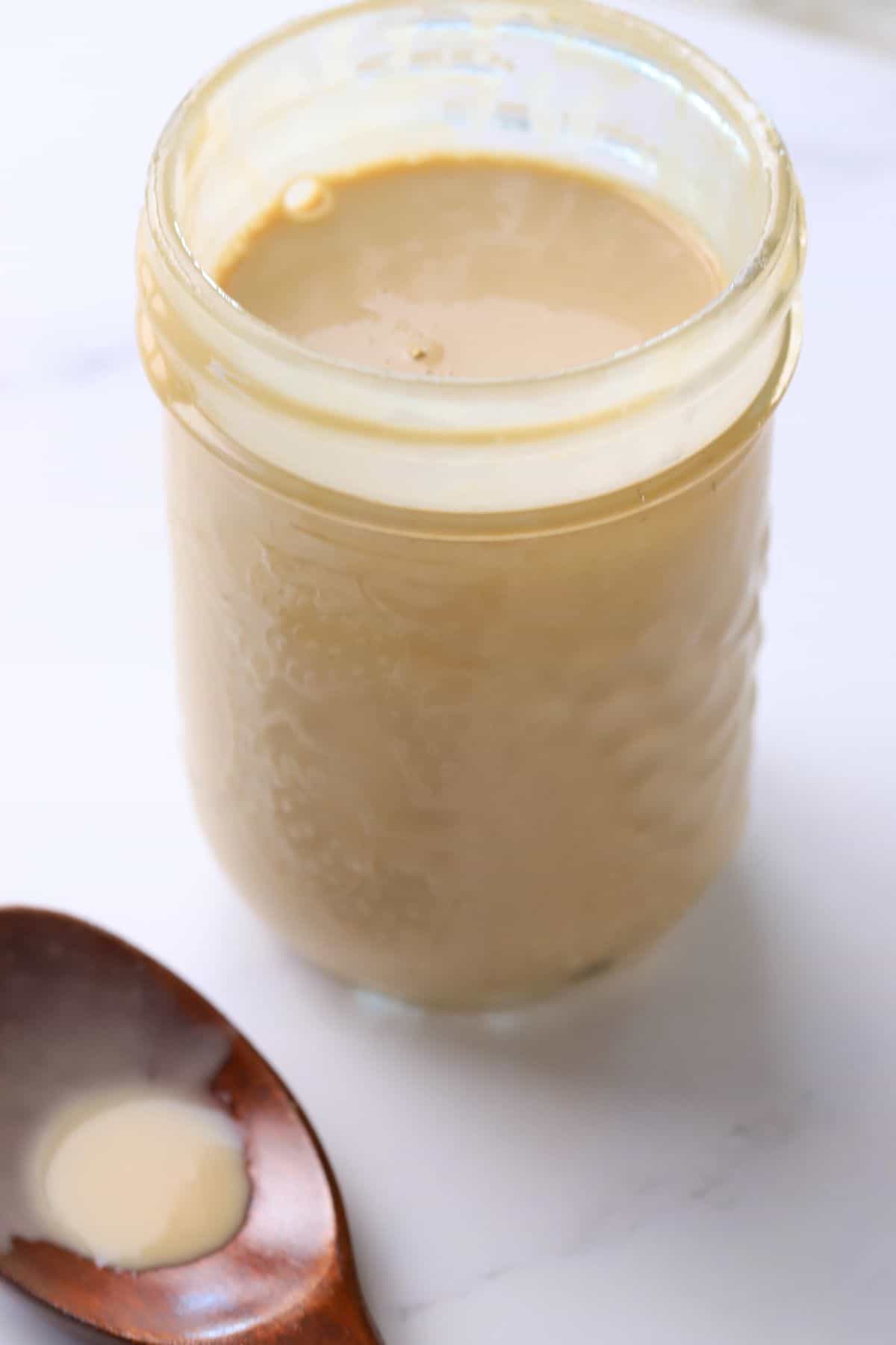 Sugar free salad dressing in a jar next to a wooden spoon.