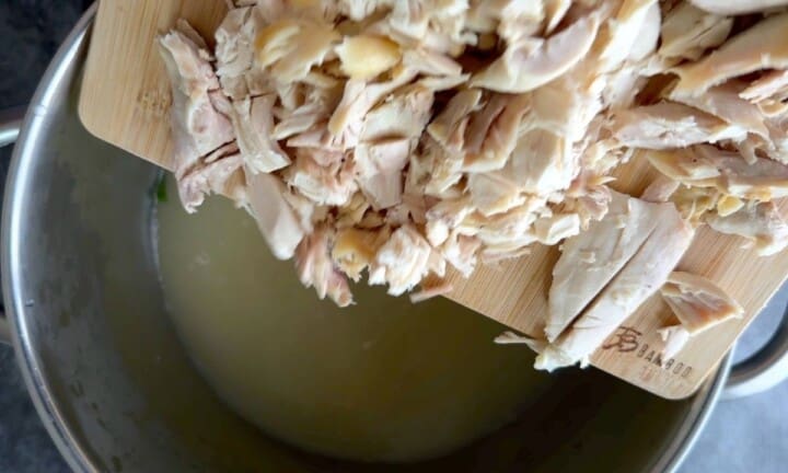 Adding shredded chicken to the soup pot.