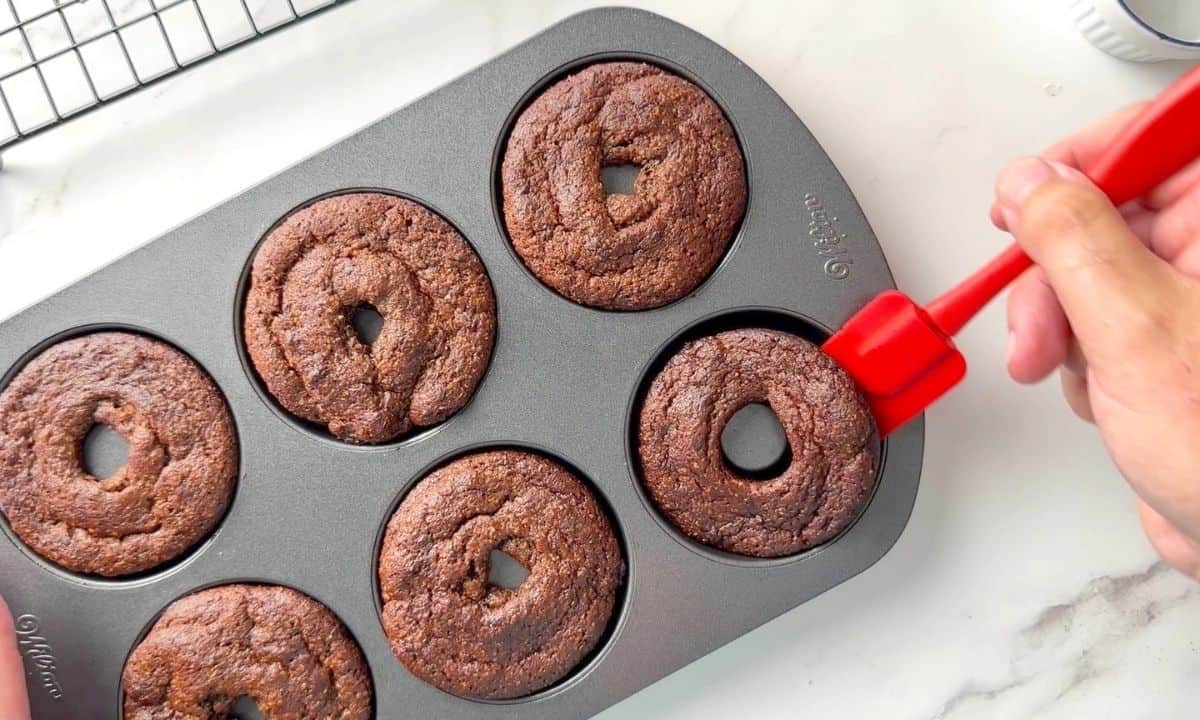 Releasing the baked donuts from the donut pan with a small red rubber spatula.