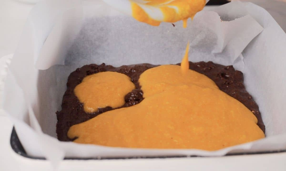 Pouring the pumpkin batter onto the chocolate batter in the baking dish.