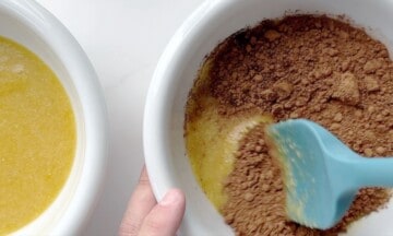 Mixing the cocoa powder into the brownie batter with a blue rubber spatula.