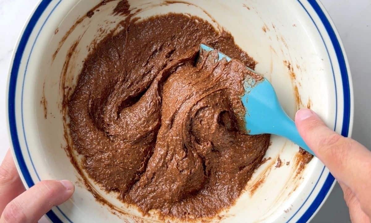 Mixing the chocolate batter in a large bowl with a blue rubber spatula.