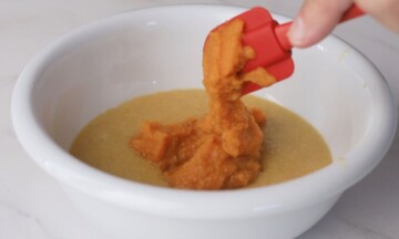 Adding the pumkin puree to the brownie batter in a white bowl.