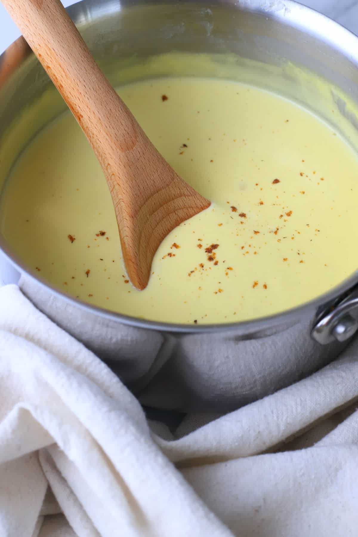 Pot full of bechamel keto sauce inserted with a wooden spoon.