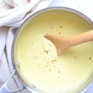 Pot full of bechamel keto sauce inserted with a wooden spoon.