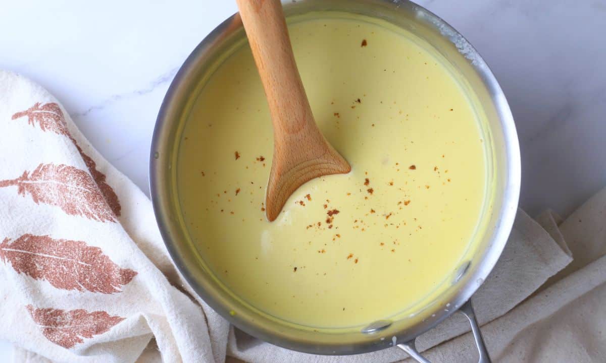 Pot full of bechamel keto sauce inserted with a wooden spoon.