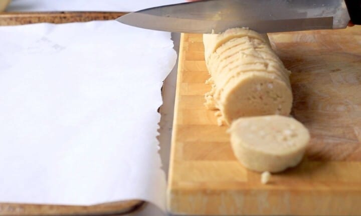 Cutting the cookie dough log into cookies with a knife on a cutting board.