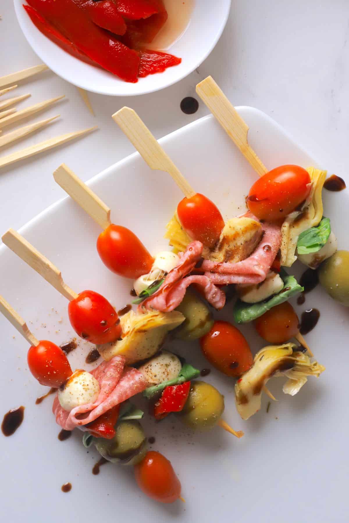 Low carb antipasto skewers on a white platter next to slices of roasted red peppers.