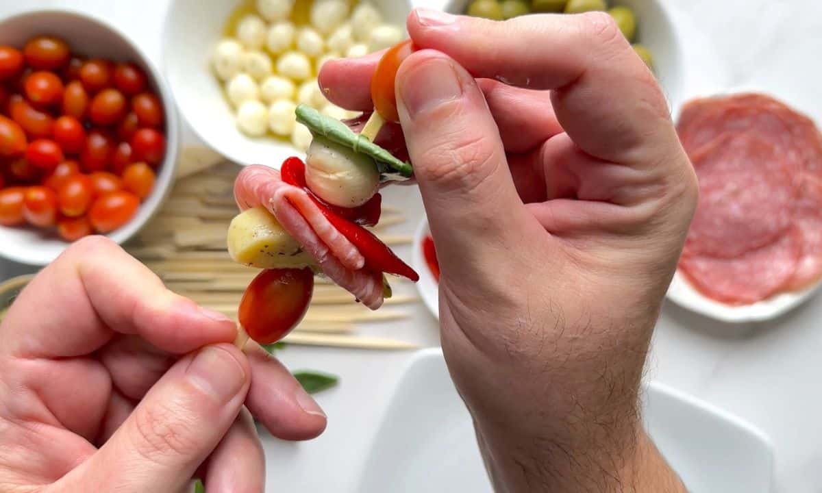 Threading a low carb antipasto skewer with the ingredients in the background.