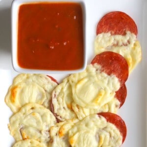 Low carb pepperoni bites on a white platter with a side of marinara sauce.