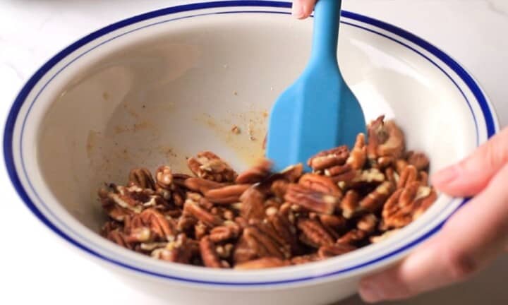 Stirring the candied pecans with the glaze in a large bowl.