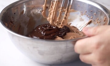 Mixing the melted chocolate into the cheesecake mixer in a bowl.