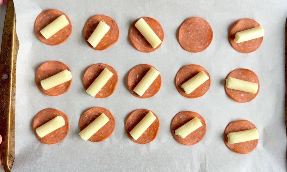 Pepperoni topped with pieces of mozzarella cheestring on a parchment lined sheet pan.