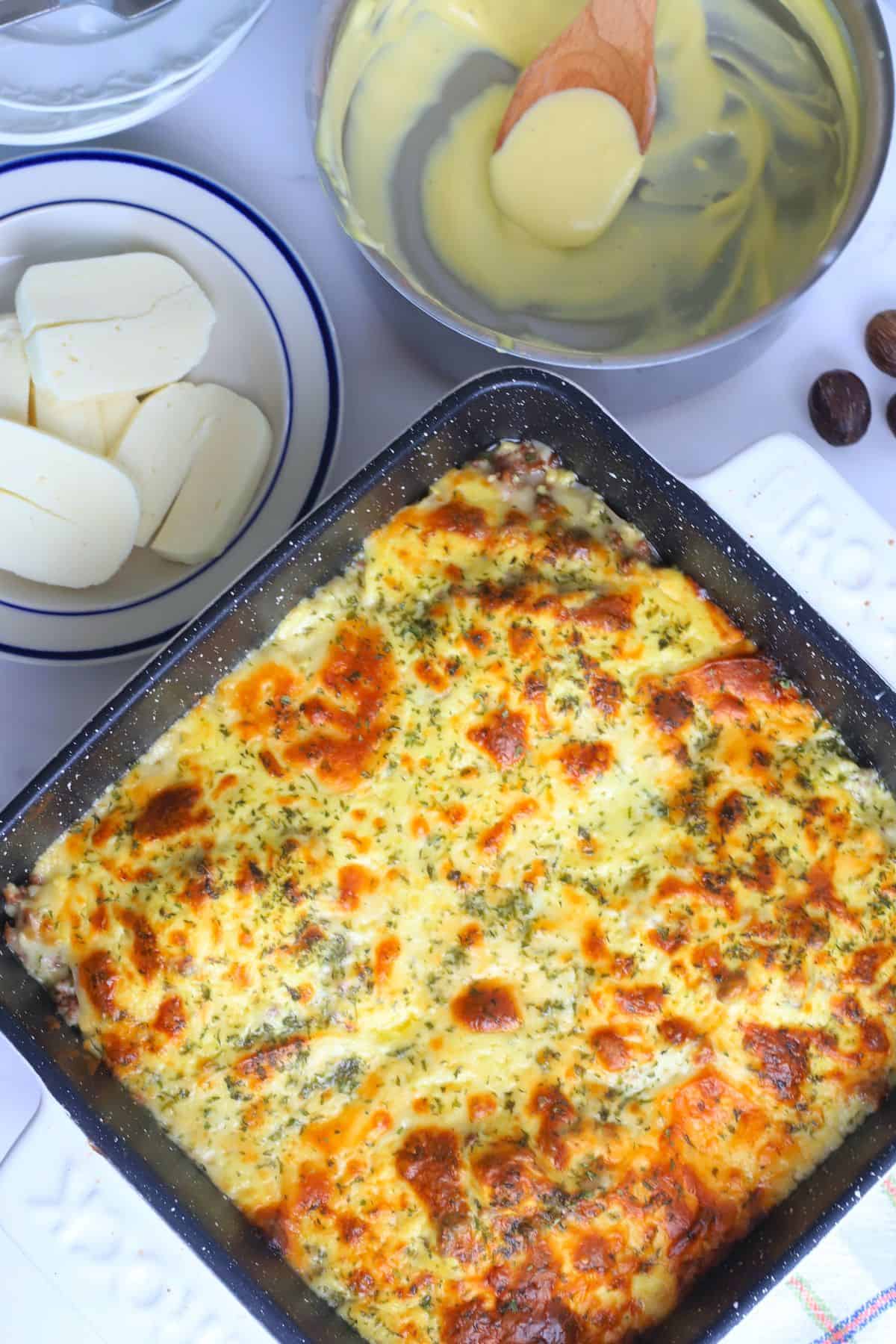 Baked low carb protein lasagne next to a plate of halloumi, bechamel sauce and nutmeg pods.