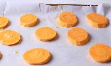 Sliced sweet potatoes on a parchment lined baking sheet.