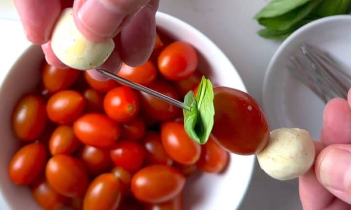 Threading a caprese skewer with bocconcini, mozzarella and basil.