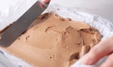 Spreading the cheesecake filling over the crust in a pan lined with parchment paper.
