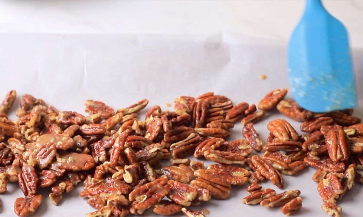Low carb candied pecans on a parchment lined baking tray with a blue rubber spatula.