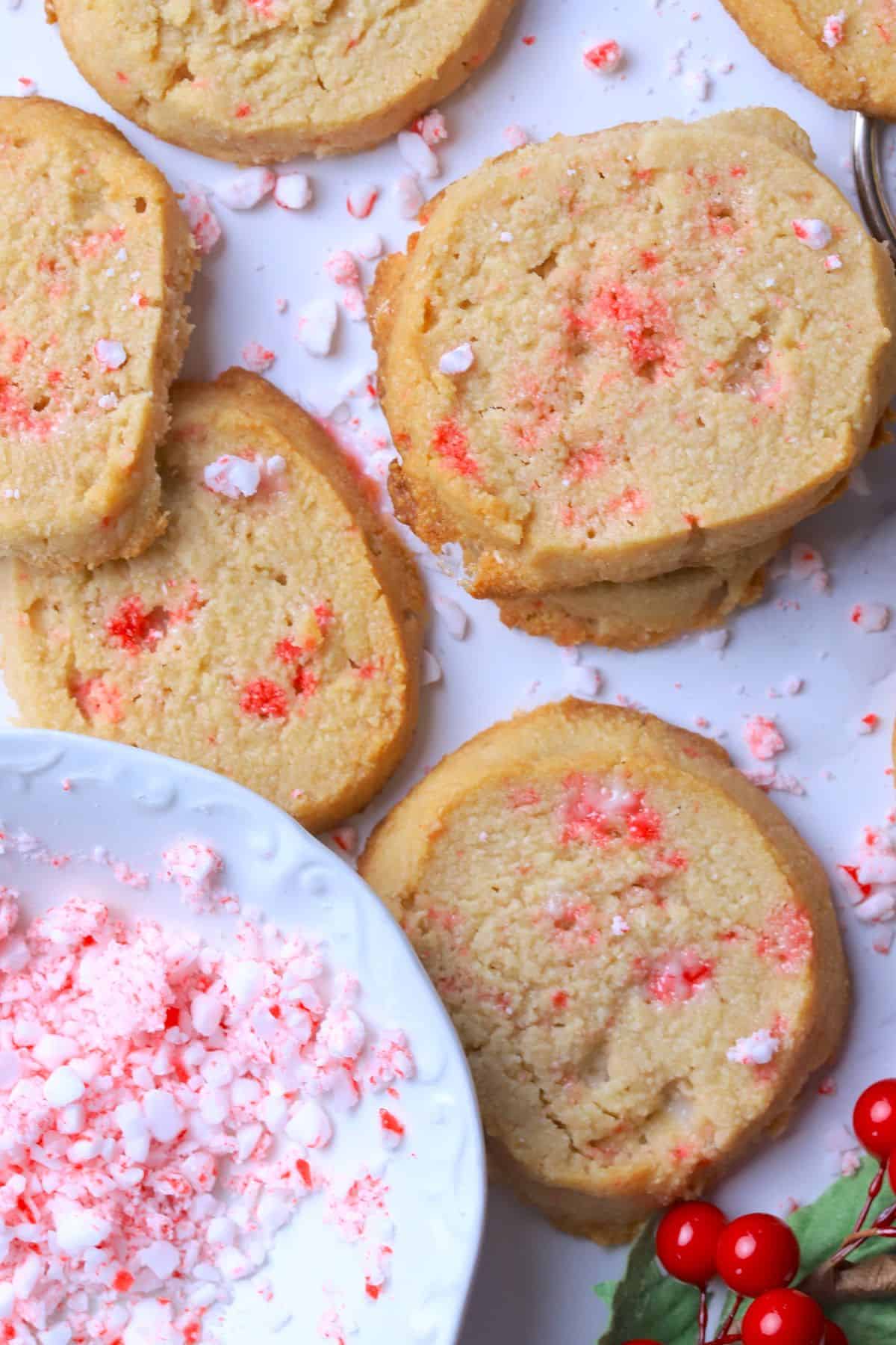 Sugar free peppermint shortbread cookies topped with crushed candy canes on a white plate next to a bowl of crushed candy canes.
