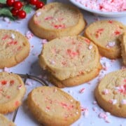 Sugar free peppermint shortbread cookies topped with crushed candy canes on a white plate next to a bowl of crushed candy canes.