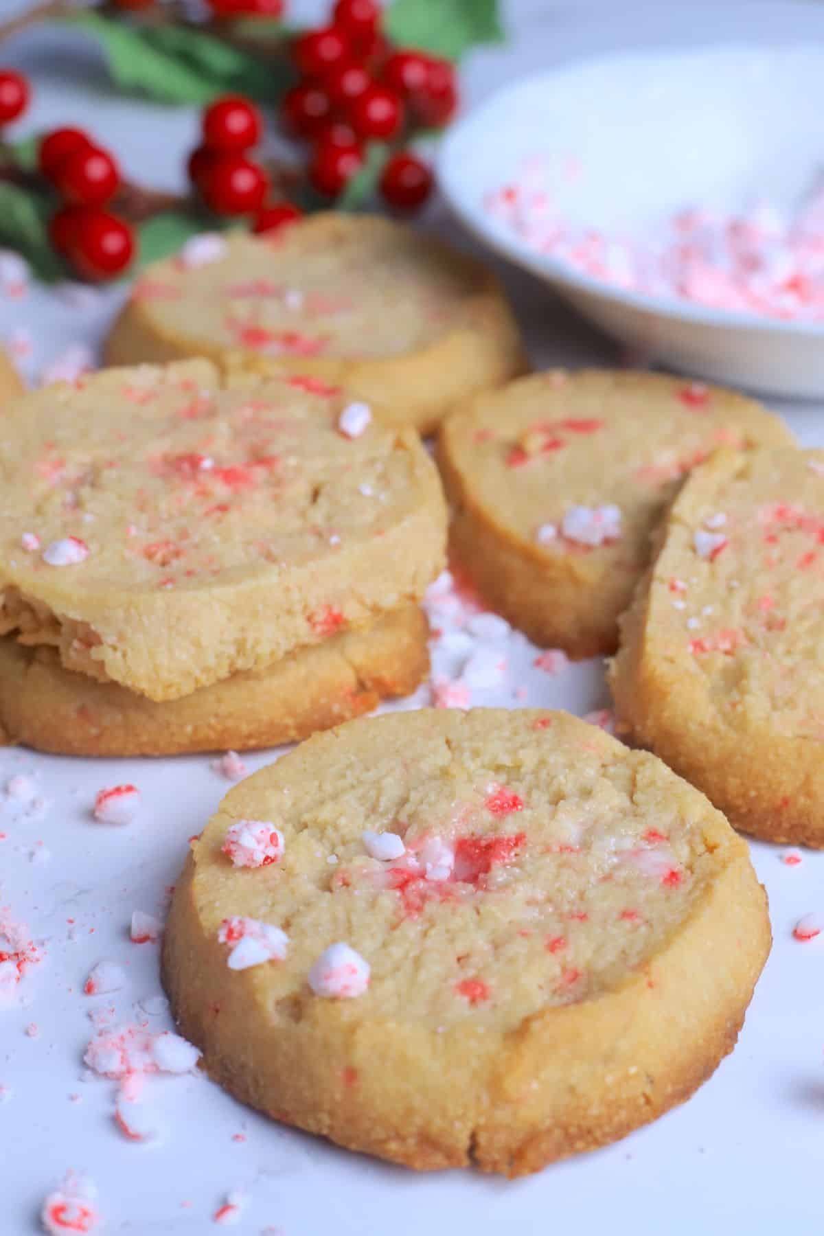 Sugar free peppermint shortbread cookies topped with crushed candy canes on a white plate next to a bowl of crushed candy canes.