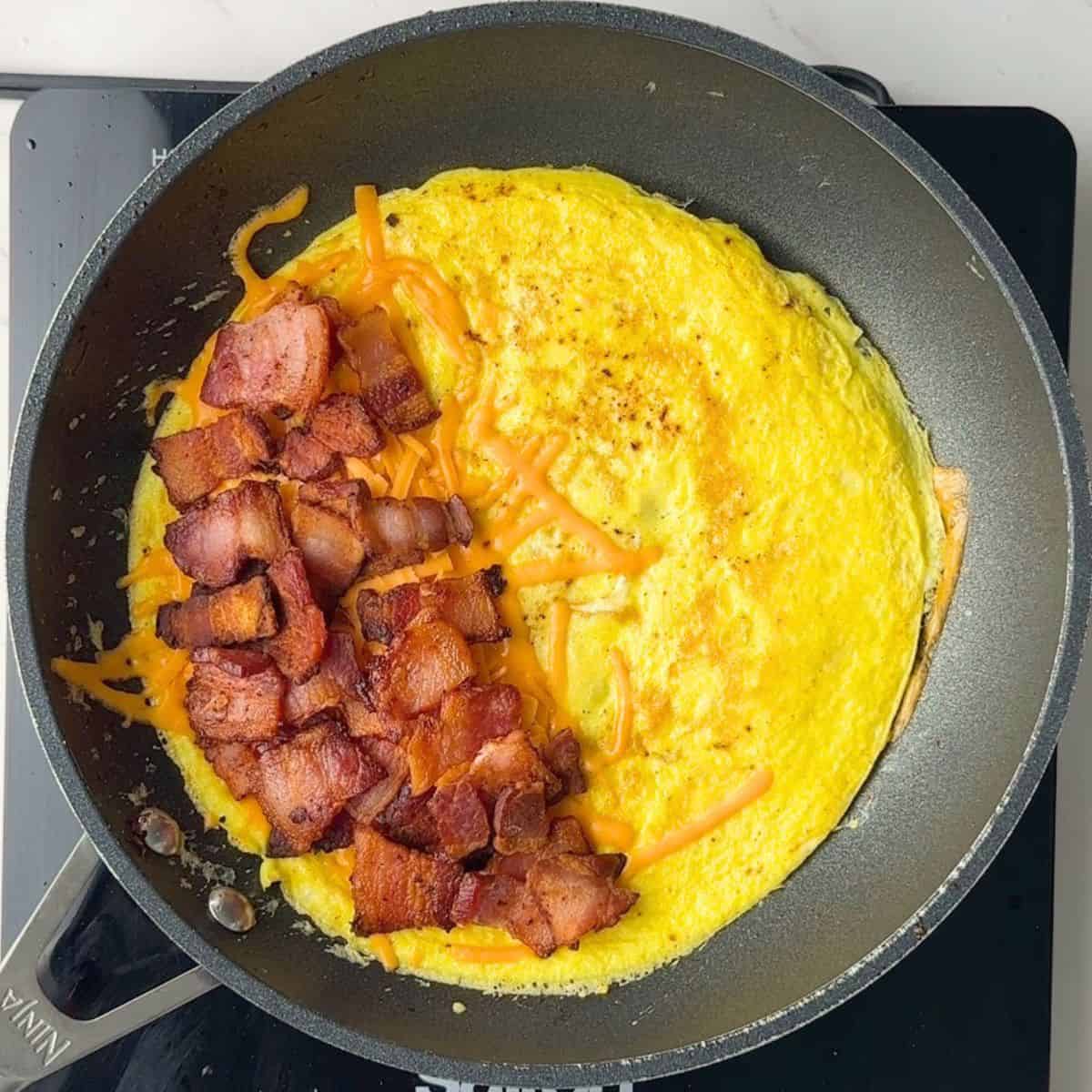 Bacon and cheese on an omlette in a skillet.